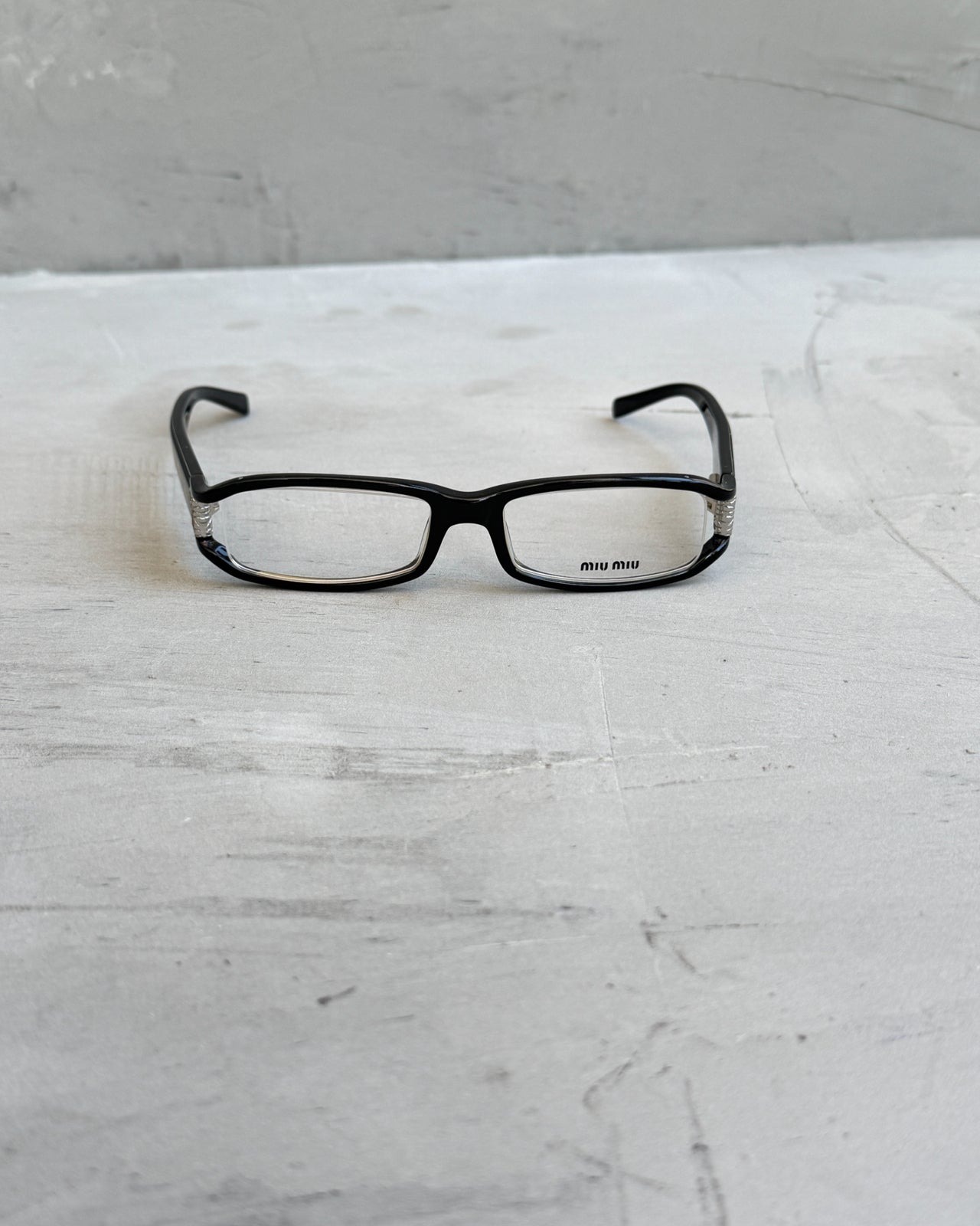 Miu Miu Black Clear Lens Glasses-on a concrete background