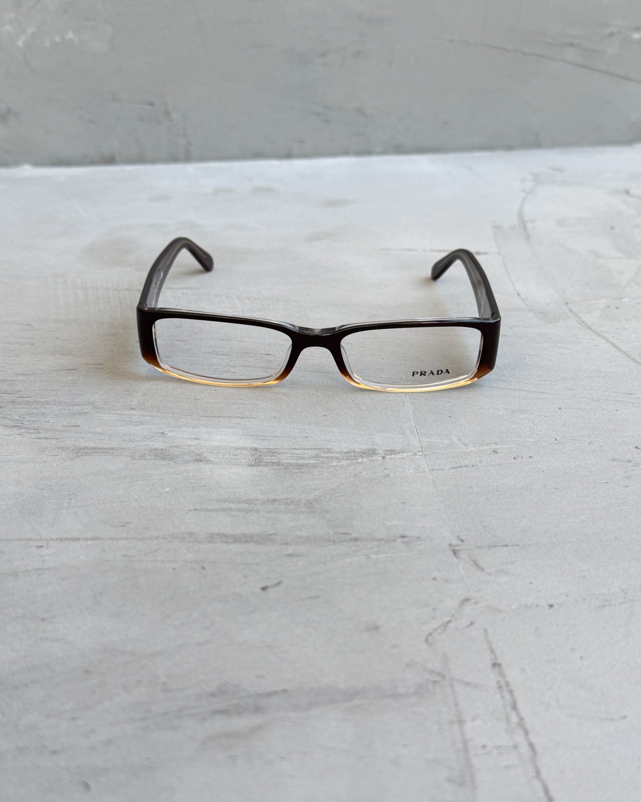 Prada Clear Lens Brown Frame Glasses-on a concrete background