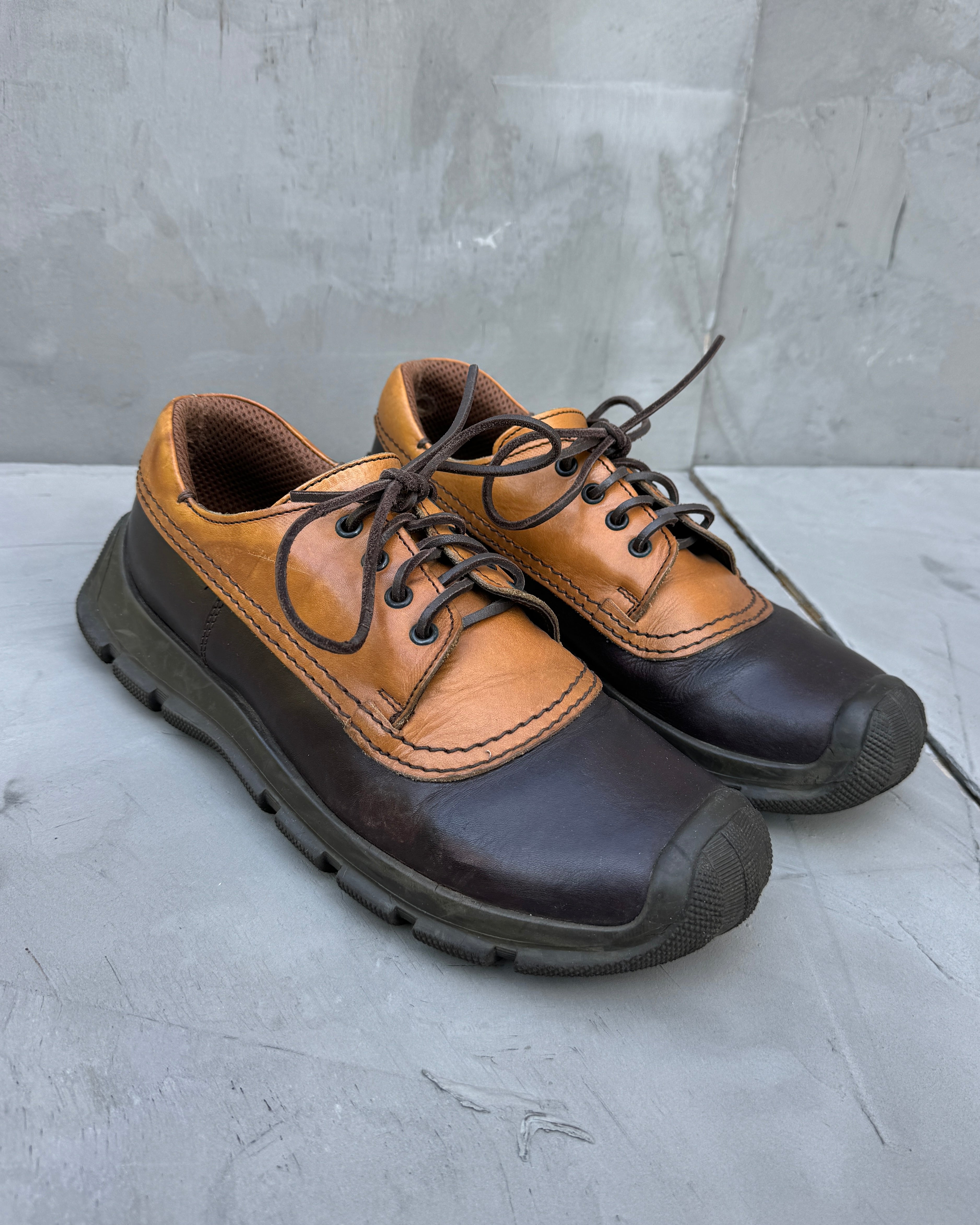 Pair of brown and black shoes on a gray surface with a concrete wall background