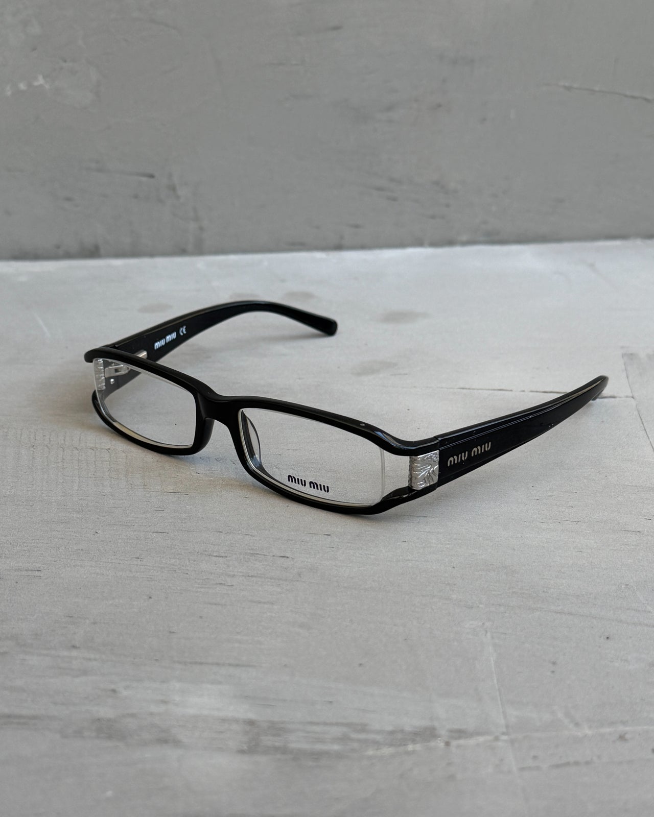 Miu Miu Black Clear Lens Glasses-on a concrete background