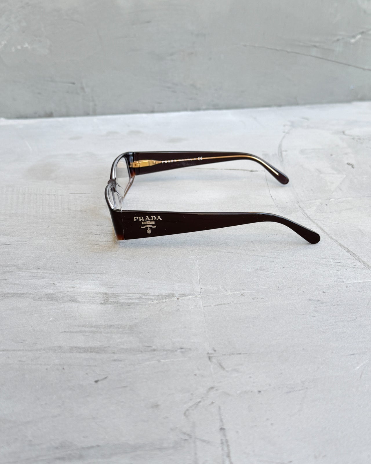 Prada Clear Lens Brown Frame Glasses-on a concrete background