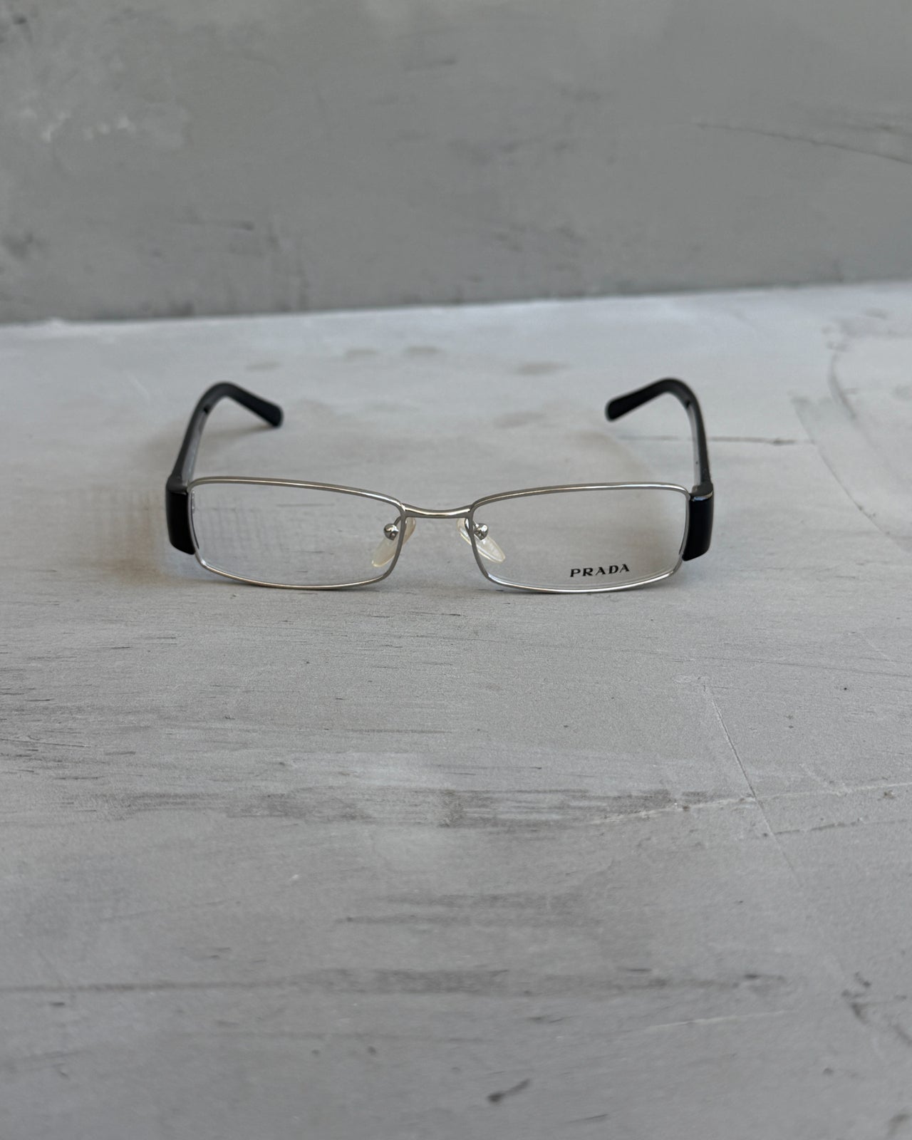 Prada Clear Lens Silver Frame Glasses-on a concrete background